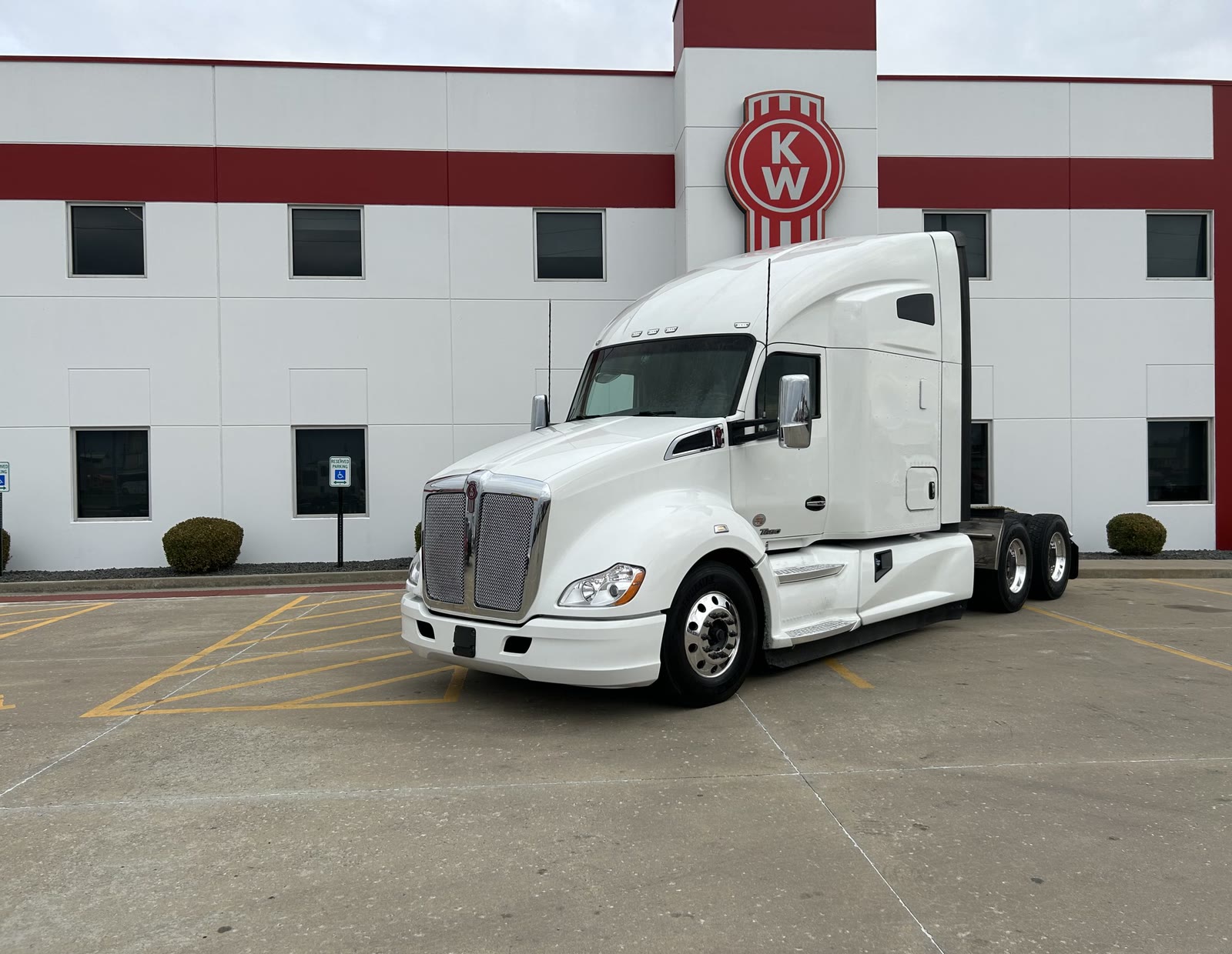 A white Kenworth T680 sleeper tractor parked outside a Kenworth facility.
